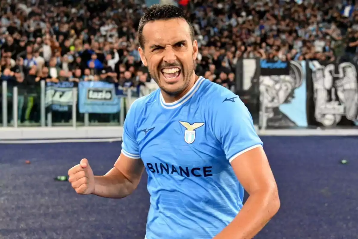 Futbolista celebrando con gesto de euforia en un estadio lleno de aficionados mientras viste el uniforme azul del Lazio Futbolista celebrando con gesto de euforia en un estadio lleno de aficionados mientras viste el uniforme azul del Lazio