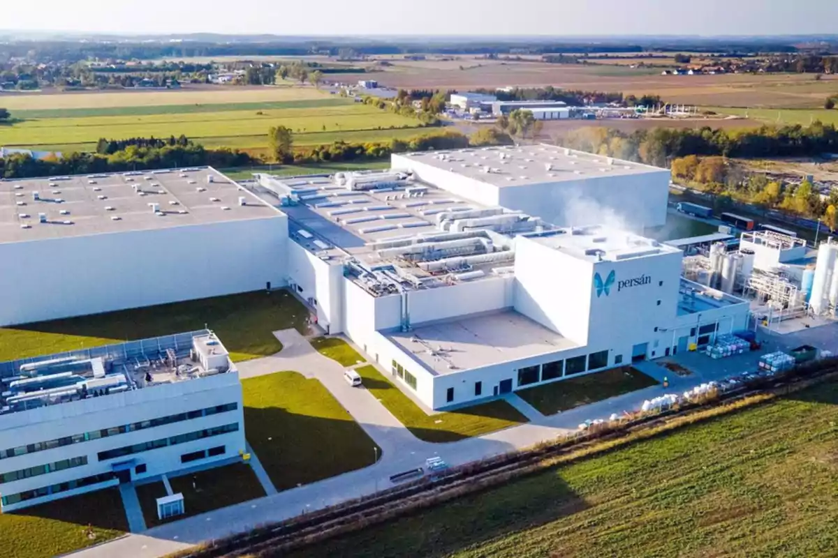 Vista aérea de una planta industrial moderna rodeada de áreas verdes y campos, con edificios blancos y el logotipo de Persán en la fachada principal