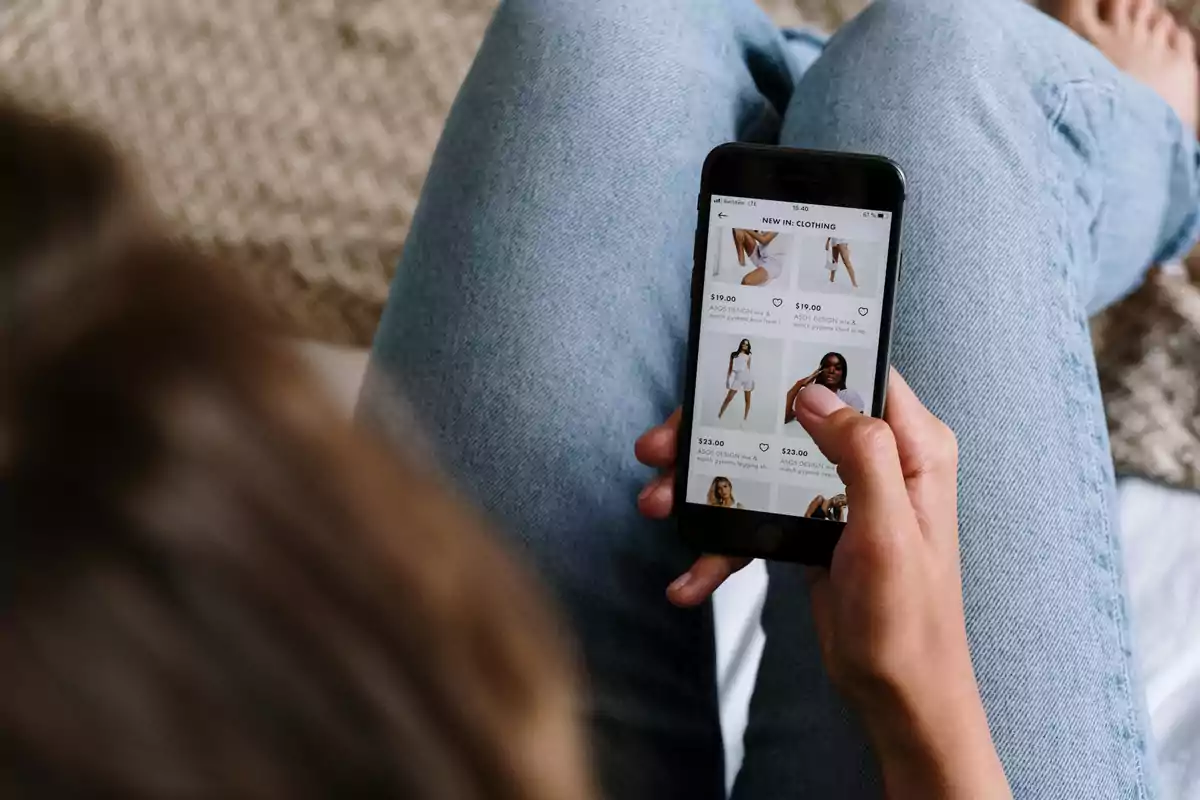 Persona sentada con jeans usando un teléfono móvil para comprar ropa en línea
