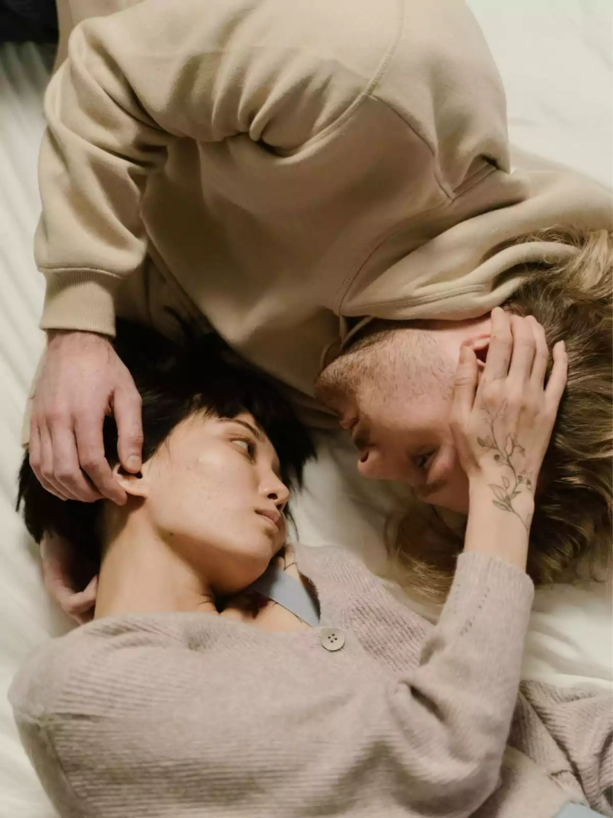 Pareja acostada mirándose a los ojos y tocándose el rostro con ternura sobre una cama Pareja acostada mirándose a los ojos y tocándose el rostro con ternura sobre una cama