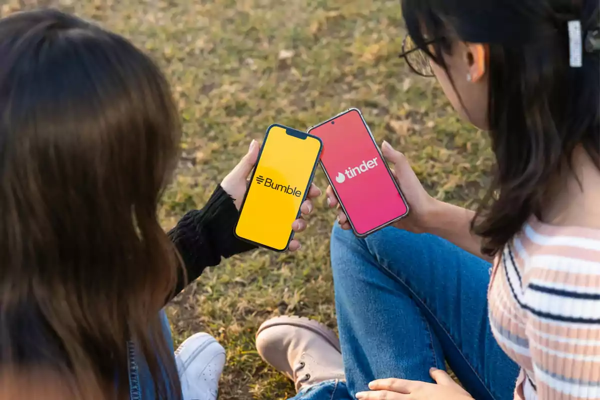 Dos mujeres sentadas en el césped sostienen teléfonos móviles que muestran las aplicaciones de Bumble y Tinder en la pantalla. Dos mujeres sentadas en el césped sostienen teléfonos móviles que muestran las aplicaciones de Bumble y Tinder en la pantalla.