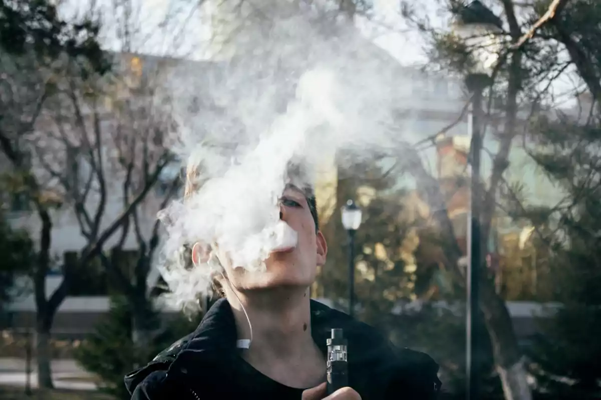 Joven usando un cigarrillo electrónico y exhalando una gran nube de vapor en un parque