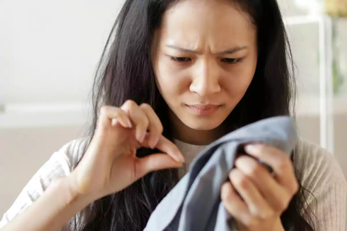 Mujer mirando con preocupación una prenda de ropa mientras intenta quitarle una pelusa Mujer mirando con preocupación una prenda de ropa mientras intenta quitarle una pelusa