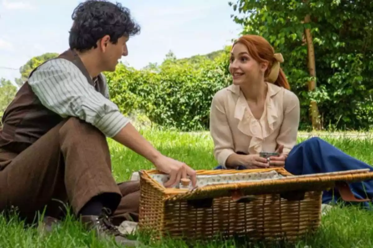 Pareja sentada en el césped disfrutando de un picnic con una canasta en un parque rodeado de árboles y vegetación Pareja sentada en el césped disfrutando de un picnic con una canasta en un parque rodeado de árboles y vegetación