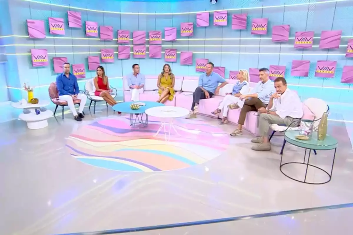 Un grupo de personas sentadas en un set de televisión moderno que pertenece a 'Vamos a Ver' con decoración en tonos pastel y varios letreros en la pared.