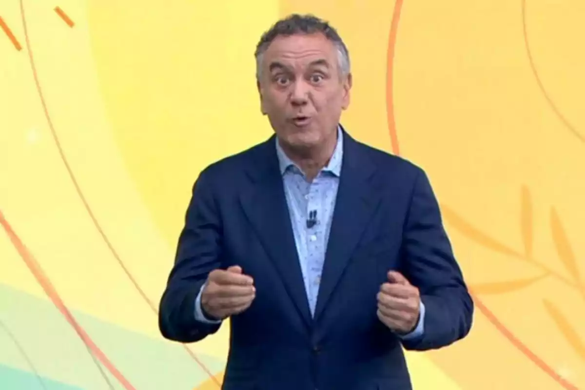 Plano medio de Roberto Brasero vestido con un traje azul y una camisa clara gesticulando frente a un fondo amarillo con líneas curvas. Plano medio de Roberto Brasero vestido con un traje azul y una camisa clara gesticulando frente a un fondo amarillo con líneas curvas.