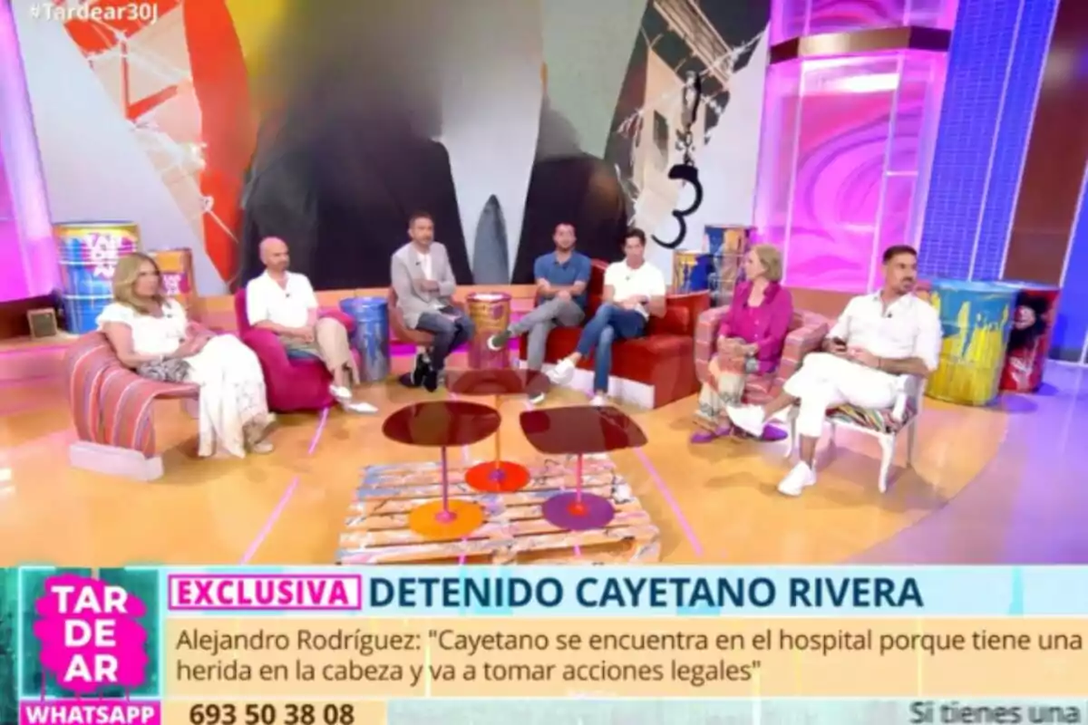 Un grupo de seis personas está sentado en un colorido set de televisión participando en un programa de tertulia, con una pantalla grande al fondo y un cintillo informativo en la parte inferior que menciona la detención de Cayetano Rivera.