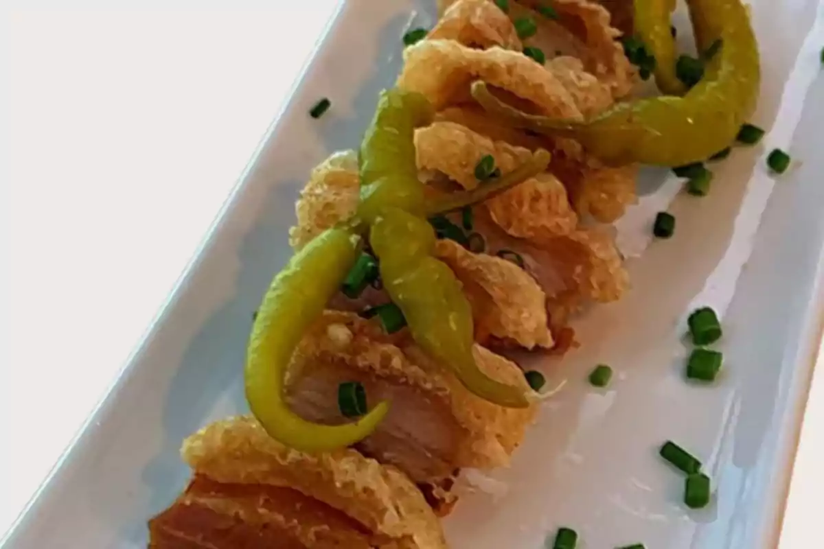 Plato de chicharrón crujiente acompañado de chiles en vinagre y espolvoreado con cebollín picado sobre un plato rectangular blanco Plato de chicharrón crujiente acompañado de chiles en vinagre y espolvoreado con cebollín picado sobre un plato rectangular blanco