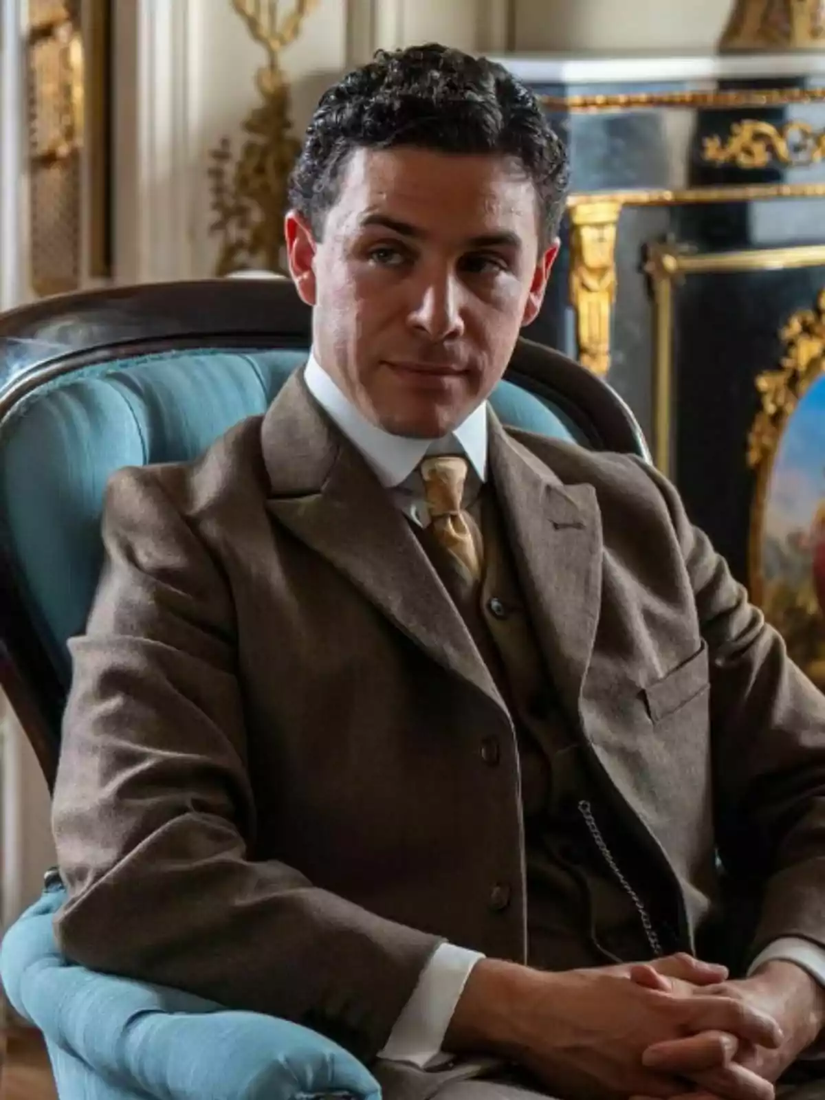 Pepe Nufrio sentado en un sillón azul, vestido con un traje marrón elegante y corbata beige, en una habitación decorada de estilo clásico Pepe Nufrio sentado en un sillón azul, vestido con un traje marrón elegante y corbata beige, en una habitación decorada de estilo clásico