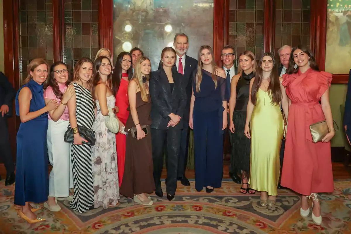 Un grupo de personas elegantemente vestidas posando juntas en el interior de un salón decorado con alfombra y vitrales. Un grupo de personas elegantemente vestidas posando juntas en el interior de un salón decorado con alfombra y vitrales.