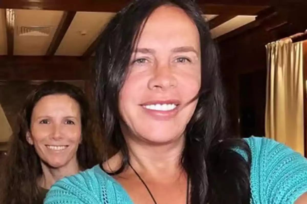 Dos mujeres sonríen mientras posan para una selfie en una habitación con cortinas claras y techo de madera. Dos mujeres sonríen mientras posan para una selfie en una habitación con cortinas claras y techo de madera.