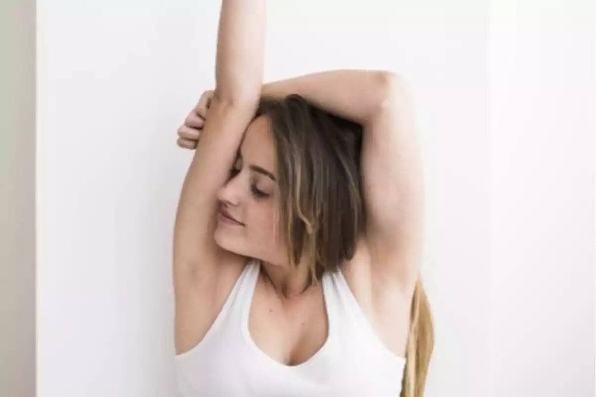 Mujer joven con camiseta blanca levantando un brazo y oliendo su axila