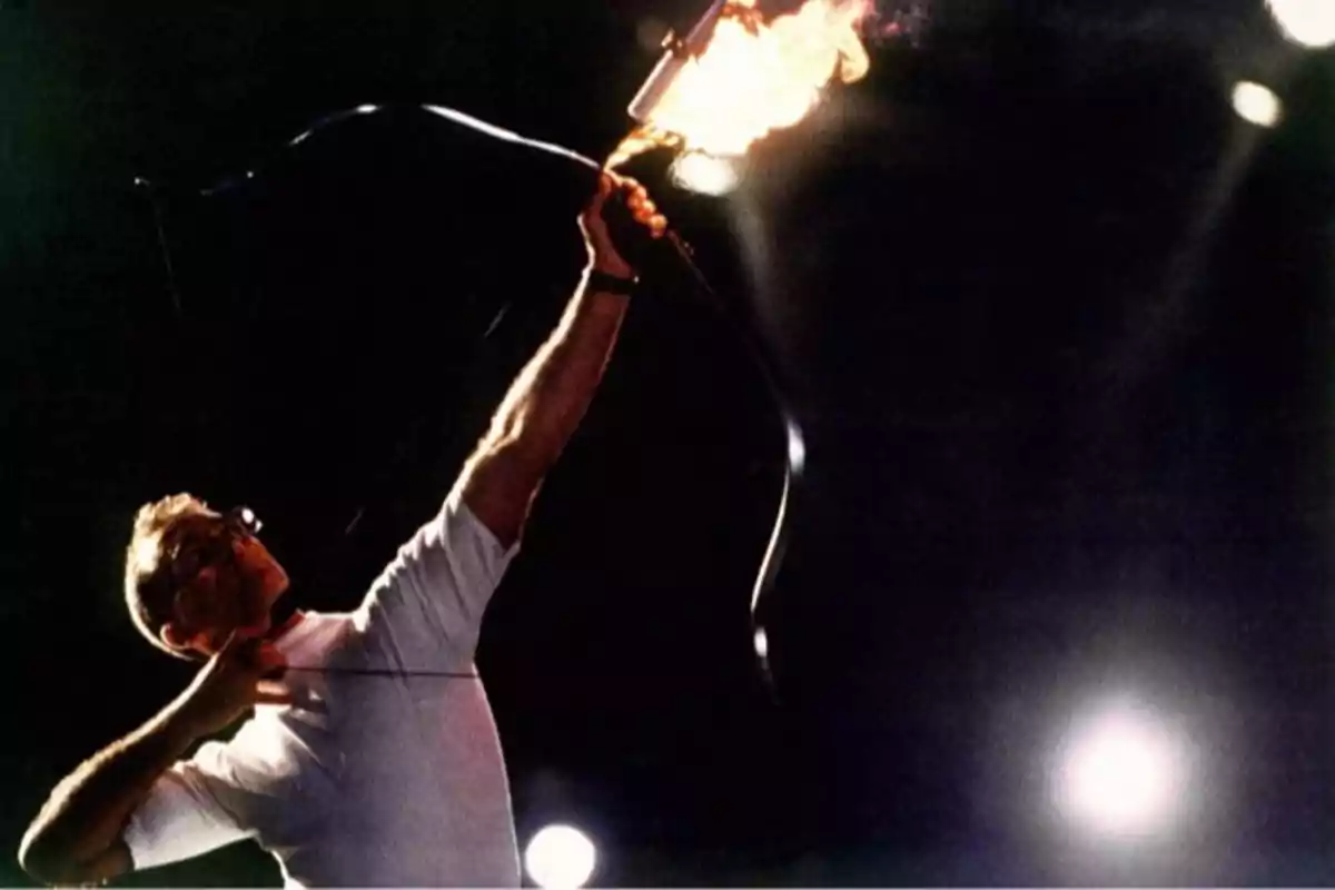 Persona disparando una flecha encendida con fuego usando un arco en un entorno oscuro iluminado por focos. Persona disparando una flecha encendida con fuego usando un arco en un entorno oscuro iluminado por focos.