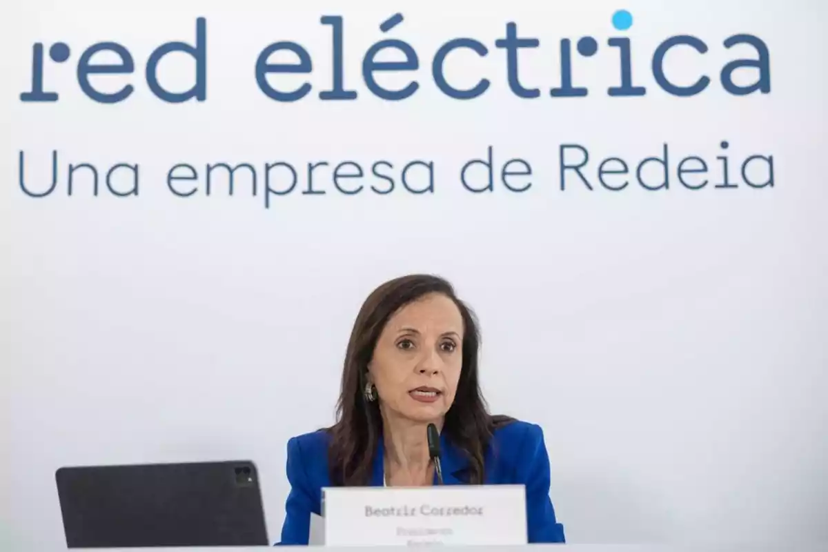 Mujer con chaqueta azul hablando en una conferencia de prensa frente a un cartel que dice red eléctrica una empresa de Redeia Mujer con chaqueta azul hablando en una conferencia de prensa frente a un cartel que dice red eléctrica una empresa de Redeia