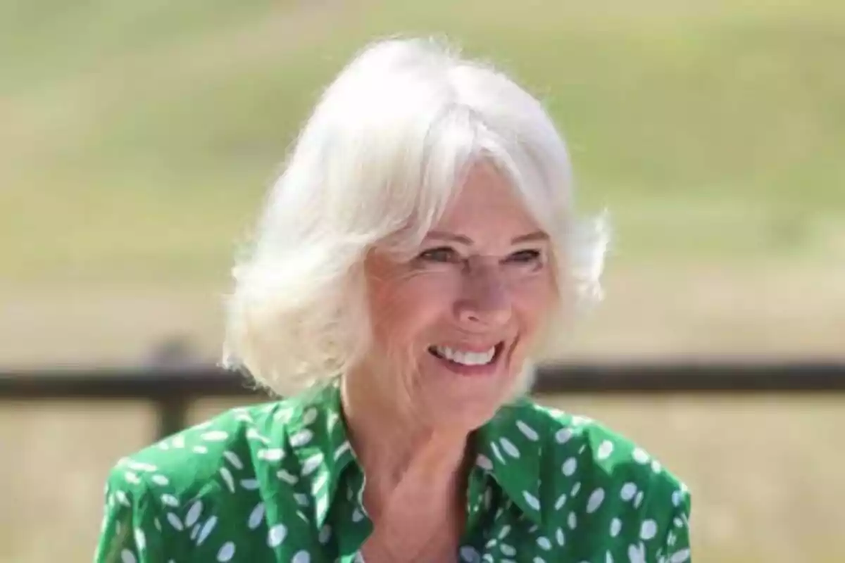 Plano corto de la reina Camila sonriente mientras usa una blusa verde con lunares blancos en un entorno al aire libre desenfocado. Plano corto de la reina Camila sonriente mientras usa una blusa verde con lunares blancos en un entorno al aire libre desenfocado.