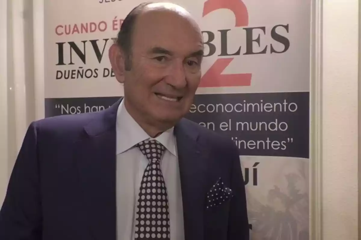Hombre de traje y corbata de lunares posando frente a un cartel promocional de un evento o conferencia