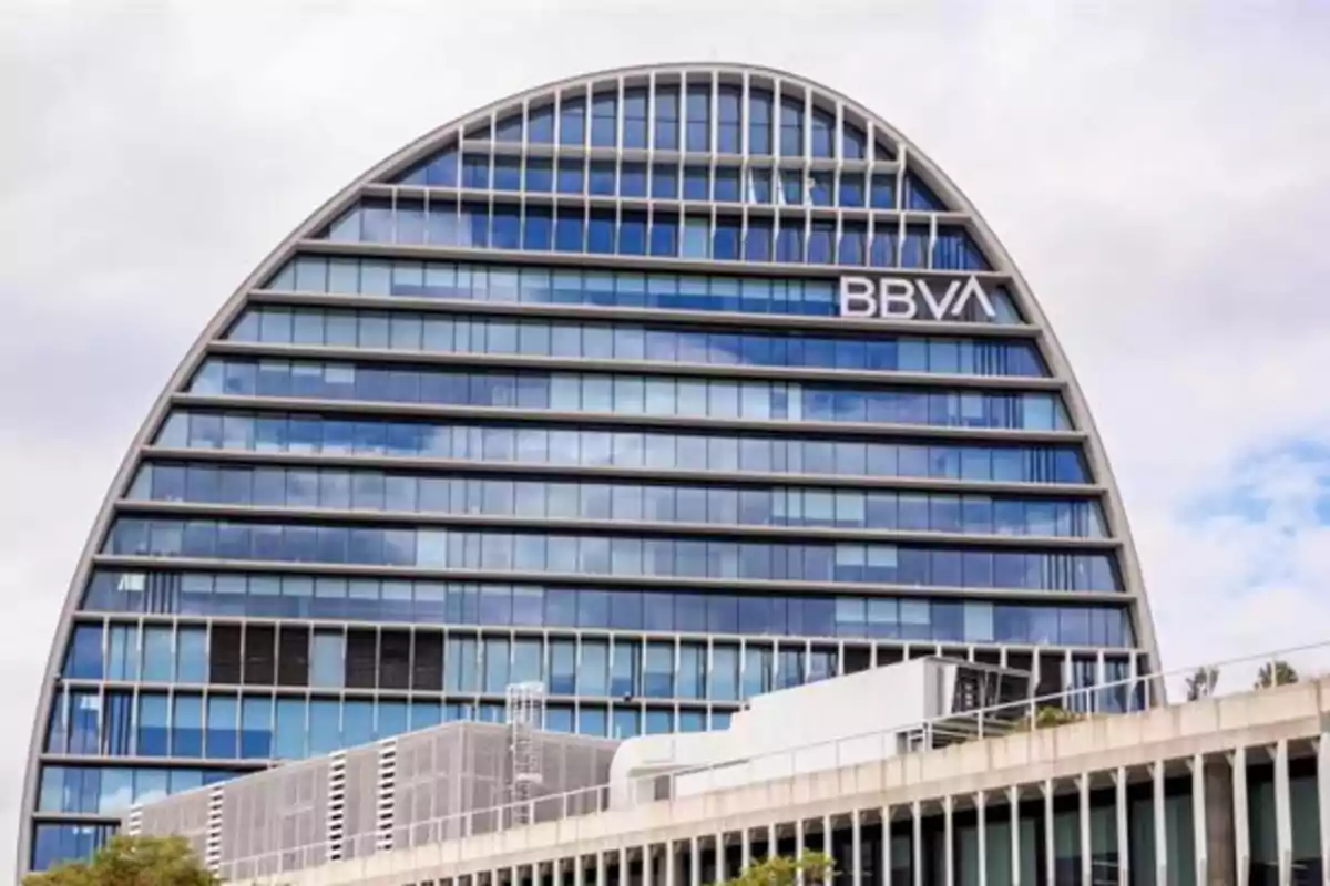 Edificio moderno de oficinas con forma semicircular y fachada de vidrio donde se observa el logo de BBVA
