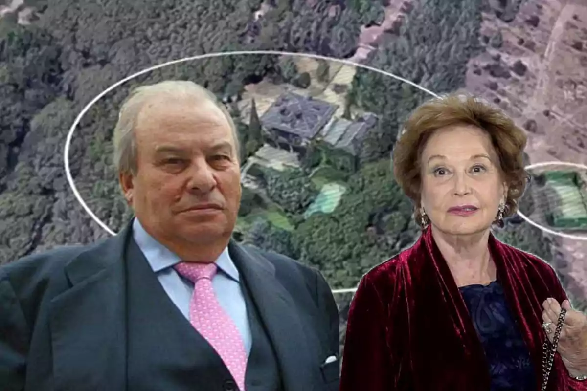 Un hombre de traje y corbata rosa junto a una mujer mayor con chaqueta de terciopelo rojo posan frente a una vista aérea de una mansión rodeada de árboles