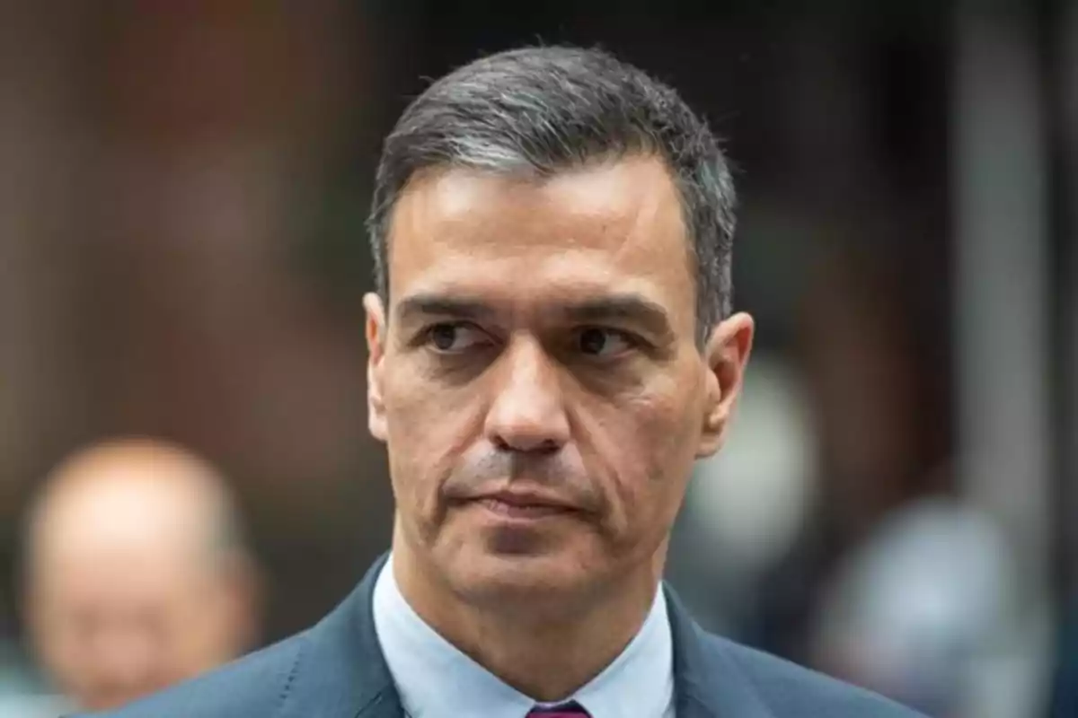 Hombre de cabello corto y canoso con expresión seria vestido con traje oscuro y corbata roja fondo desenfocado Hombre de cabello corto y canoso con expresión seria vestido con traje oscuro y corbata roja fondo desenfocado