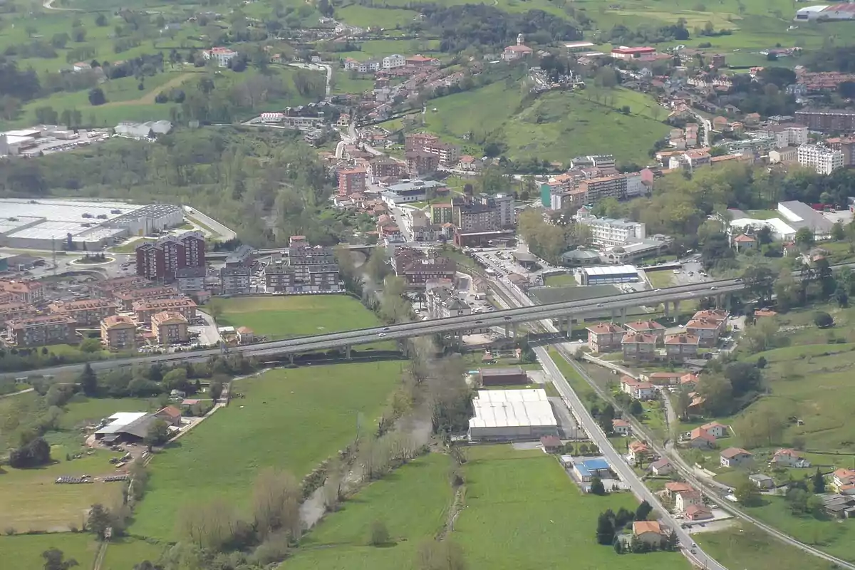Vista aérea de una ciudad rodeada de áreas verdes con edificios residenciales, carreteras y un puente elevado atravesando la zona
