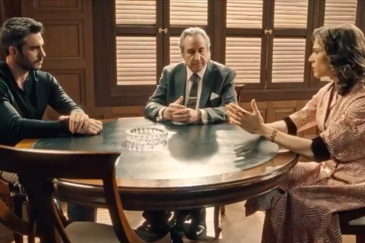 Andrés, don Pedro y Marta sentadas alrededor de una mesa redonda de madera en una habitación con ventanas de persianas, conversando de manera seria. Captura de 'Sueños de libertad' Andrés, don Pedro y Marta sentadas alrededor de una mesa redonda de madera en una habitación con ventanas de persianas, conversando de manera seria. Captura de 'Sueños de libertad'