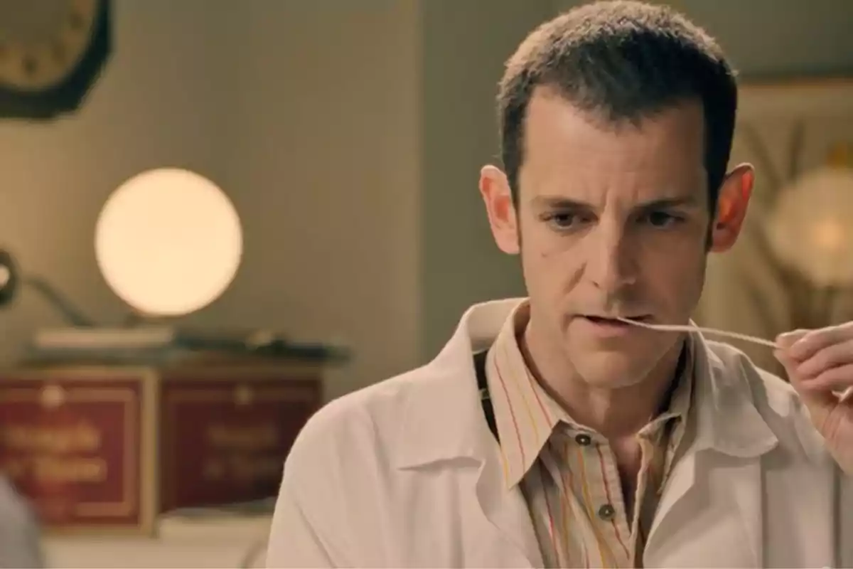 Luis con bata blanca sostiene un hisopo cerca de su boca en lo que parece ser un consultorio médico iluminado suavemente. Captura de 'sueños de libertad' Luis con bata blanca sostiene un hisopo cerca de su boca en lo que parece ser un consultorio médico iluminado suavemente. Captura de 'sueños de libertad'
