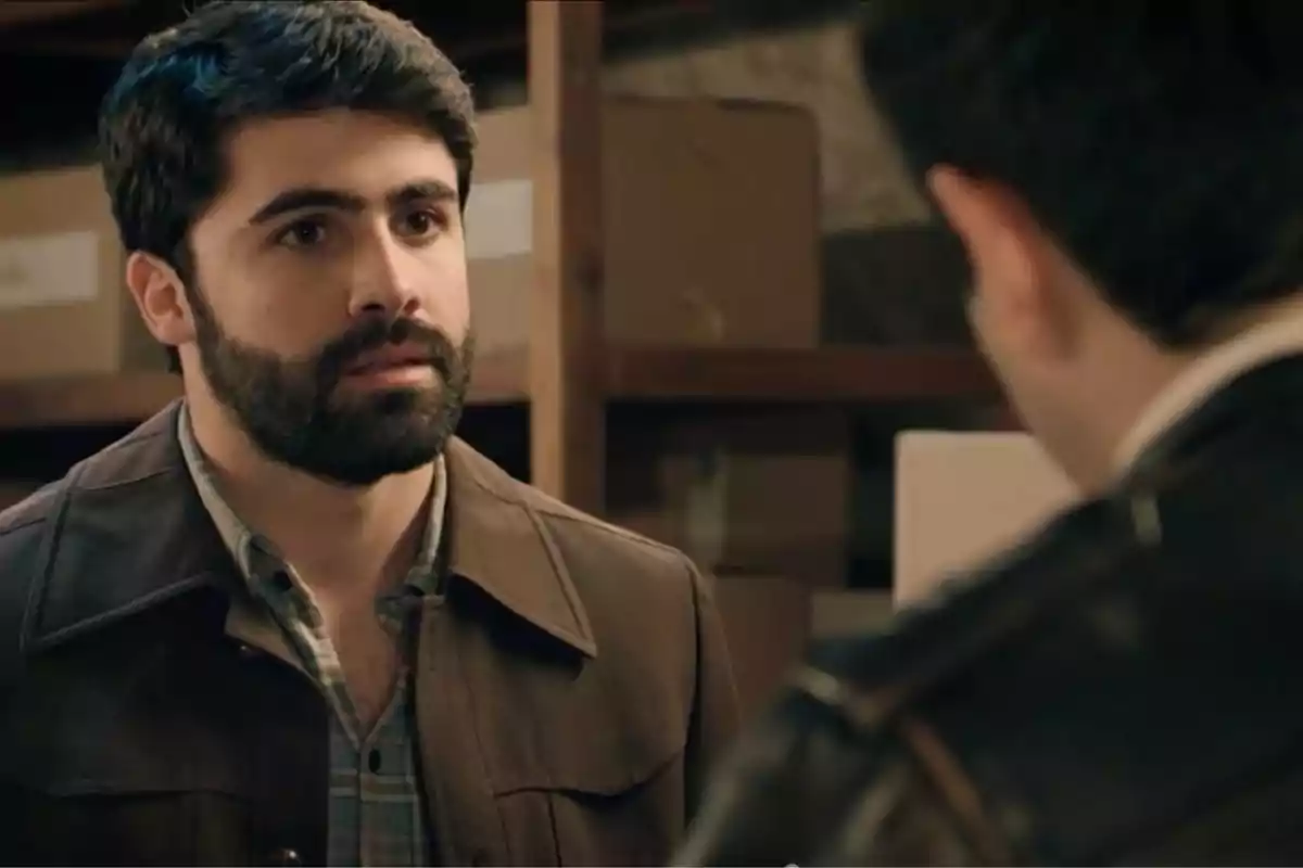 Raúl de barba y cabello oscuro con chaqueta marrón mira seriamente a otra persona en una habitación con cajas de cartón en el fondo. Captura de 'Sueños de libertad' Raúl de barba y cabello oscuro con chaqueta marrón mira seriamente a otra persona en una habitación con cajas de cartón en el fondo. Captura de 'Sueños de libertad'