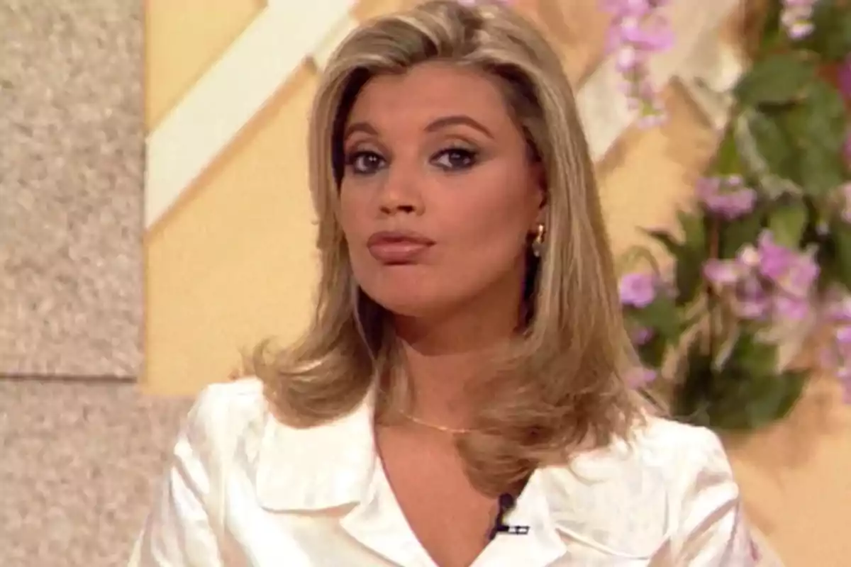 Mujer rubia con expresión seria usando blusa blanca y fondo decorado con flores moradas Mujer rubia con expresión seria usando blusa blanca y fondo decorado con flores moradas