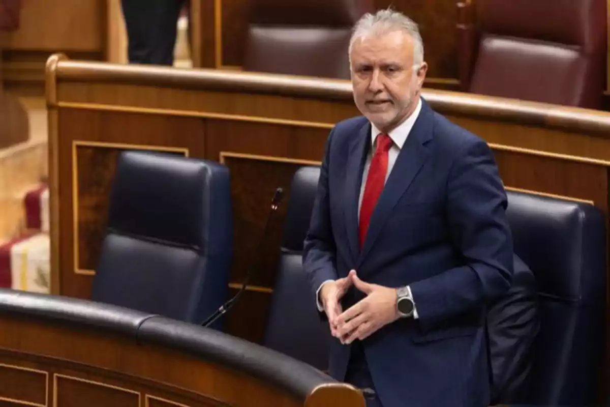 Hombre de cabello canoso con traje azul y corbata roja de pie en un parlamento o congreso Hombre de cabello canoso con traje azul y corbata roja de pie en un parlamento o congreso