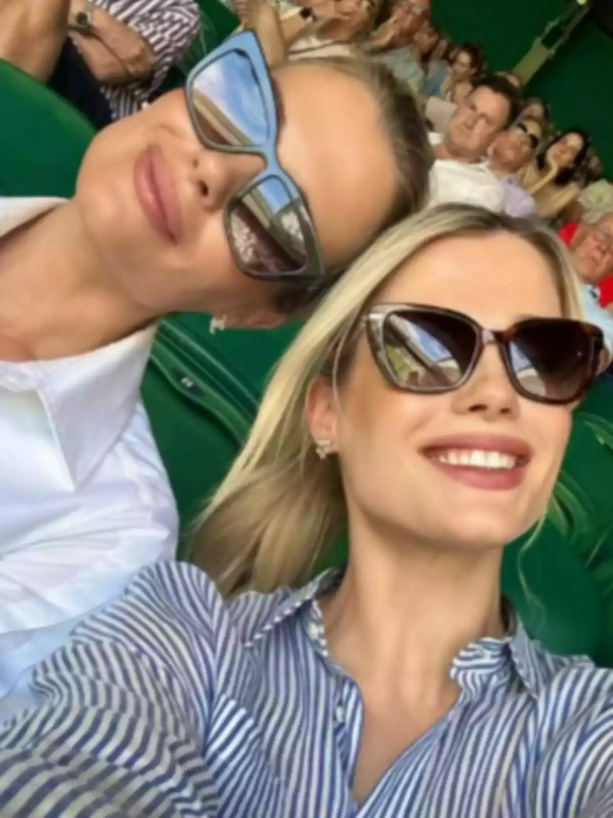 Dos mujeres sonríen usando gafas de sol, una de ellas es Amelia Spencer Mallett, mientras se toman una selfie en un estadio lleno de gente. Dos mujeres sonríen usando gafas de sol, una de ellas es Amelia Spencer Mallett, mientras se toman una selfie en un estadio lleno de gente.