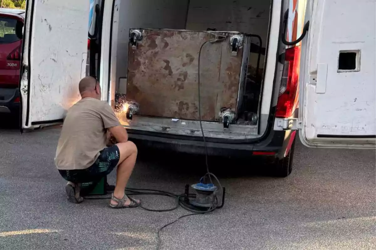 Hombre soldando una estructura metálica dentro de una camioneta con las puertas traseras abiertas en un estacionamiento Hombre soldando una estructura metálica dentro de una camioneta con las puertas traseras abiertas en un estacionamiento