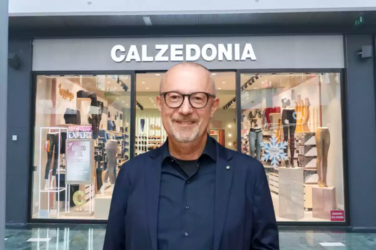 Hombre de gafas y barba sonriente posando frente a una tienda Calzedonia en un centro comercial