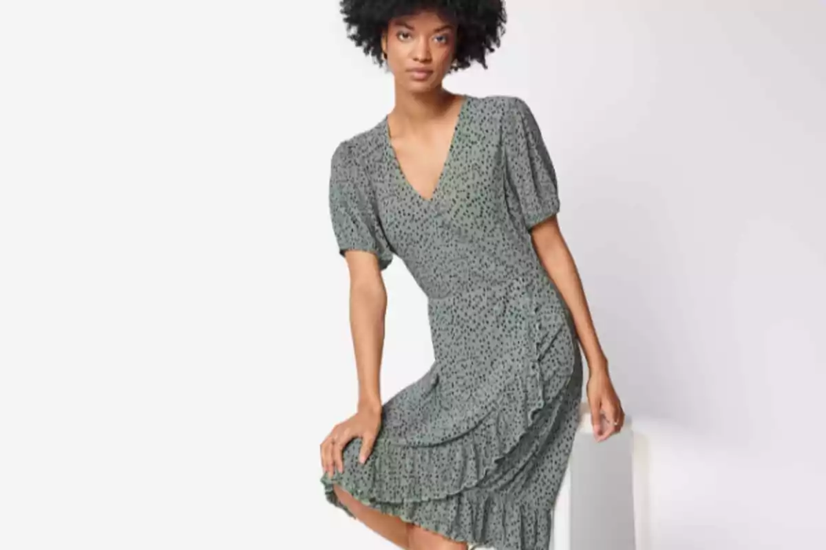 Mujer con vestido verde de manga corta y estampado de puntos pequeños sentada sobre una superficie blanca Mujer con vestido verde de manga corta y estampado de puntos pequeños sentada sobre una superficie blanca