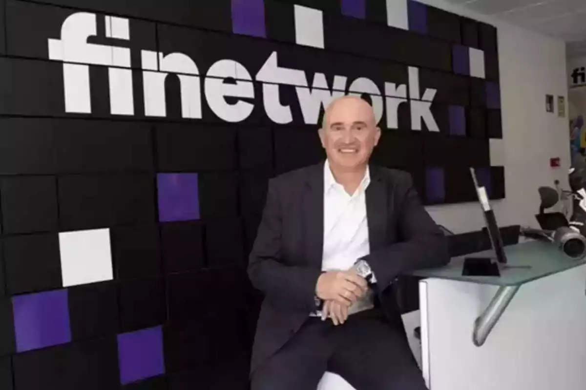 Hombre sonriente con traje sentado en una oficina moderna con el logo de finetwork en la pared de fondo Hombre sonriente con traje sentado en una oficina moderna con el logo de finetwork en la pared de fondo