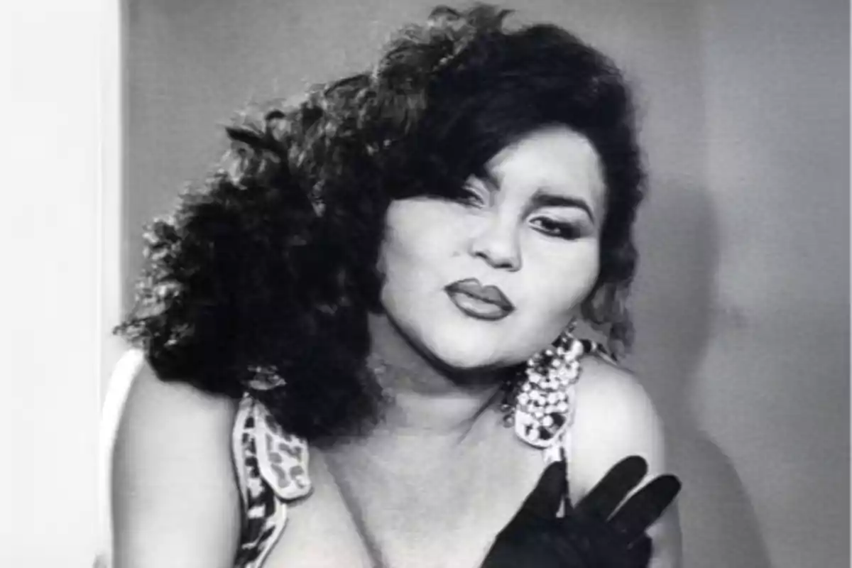 Mujer con cabello rizado y voluminoso, usando aretes grandes y guantes negros, mirando de frente en una fotografía en blanco y negro