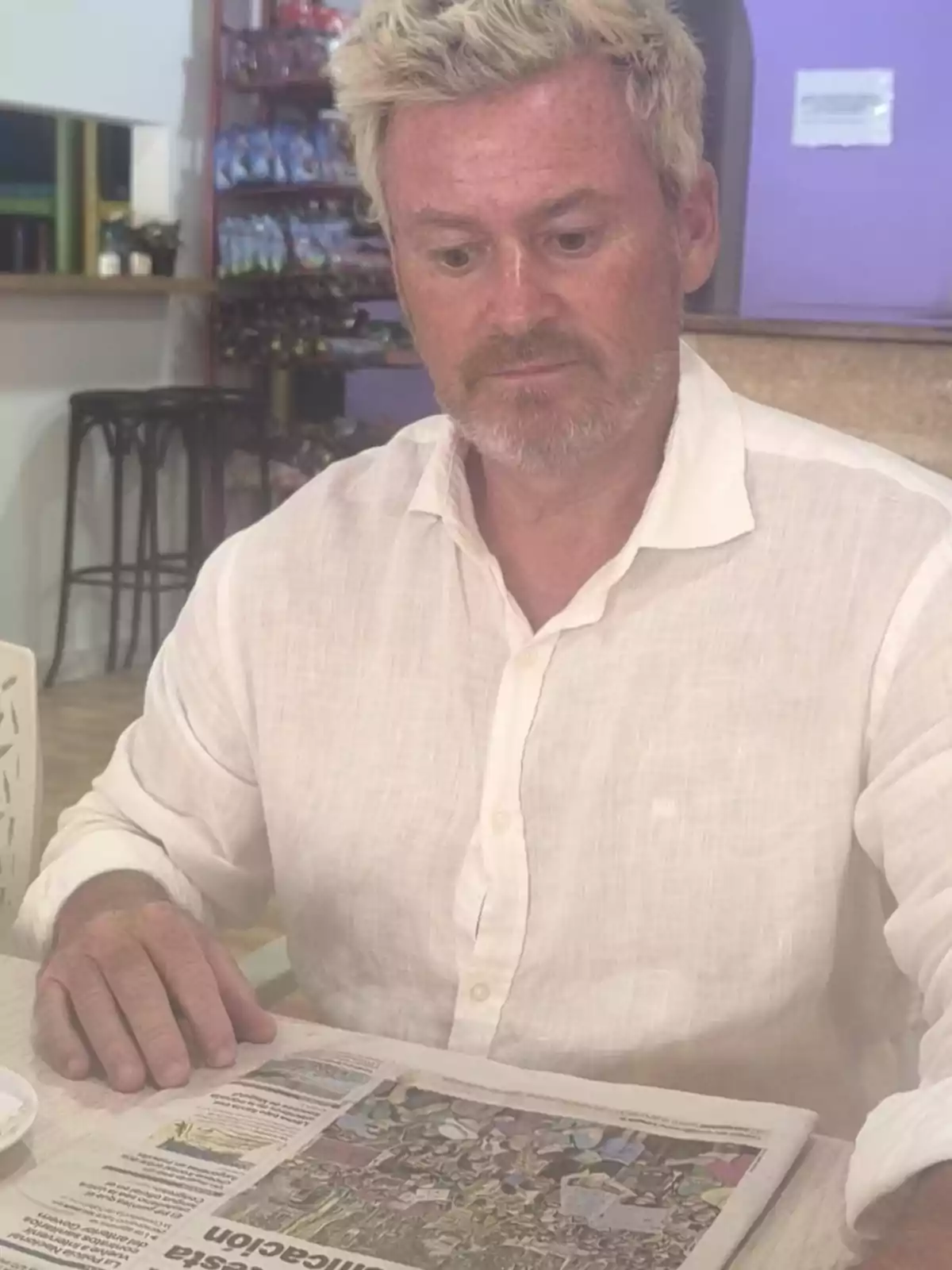 Hombre de cabello rubio y barba clara leyendo un periódico en una cafetería Hombre de cabello rubio y barba clara leyendo un periódico en una cafetería