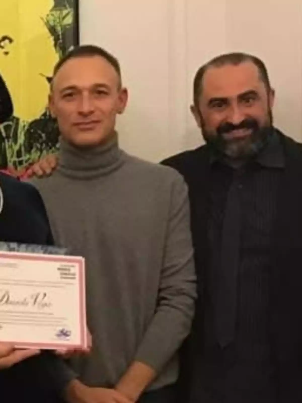 Dos hombres posan juntos en un ambiente interior uno de ellos sostiene un diploma Dos hombres posan juntos en un ambiente interior uno de ellos sostiene un diploma
