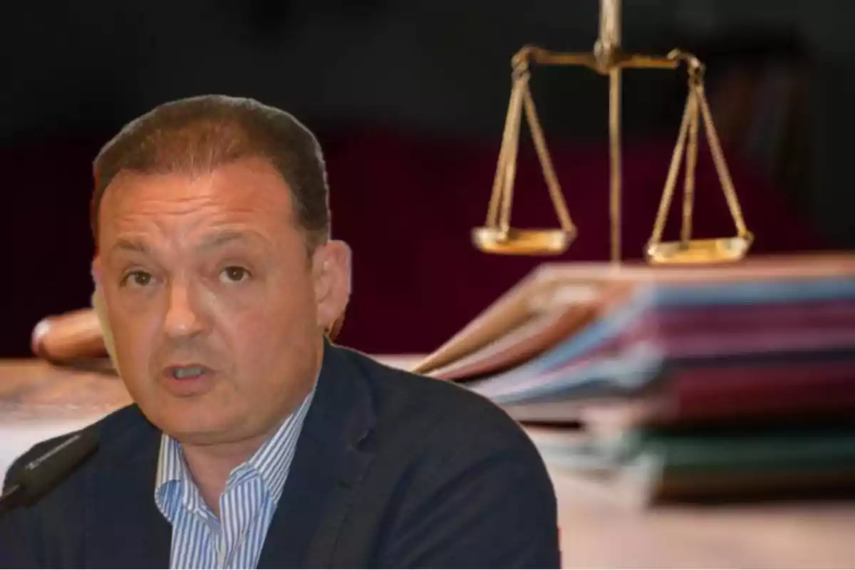 Hombre de mediana edad con expresión seria frente a un micrófono con balanza de la justicia y documentos desenfocados al fondo