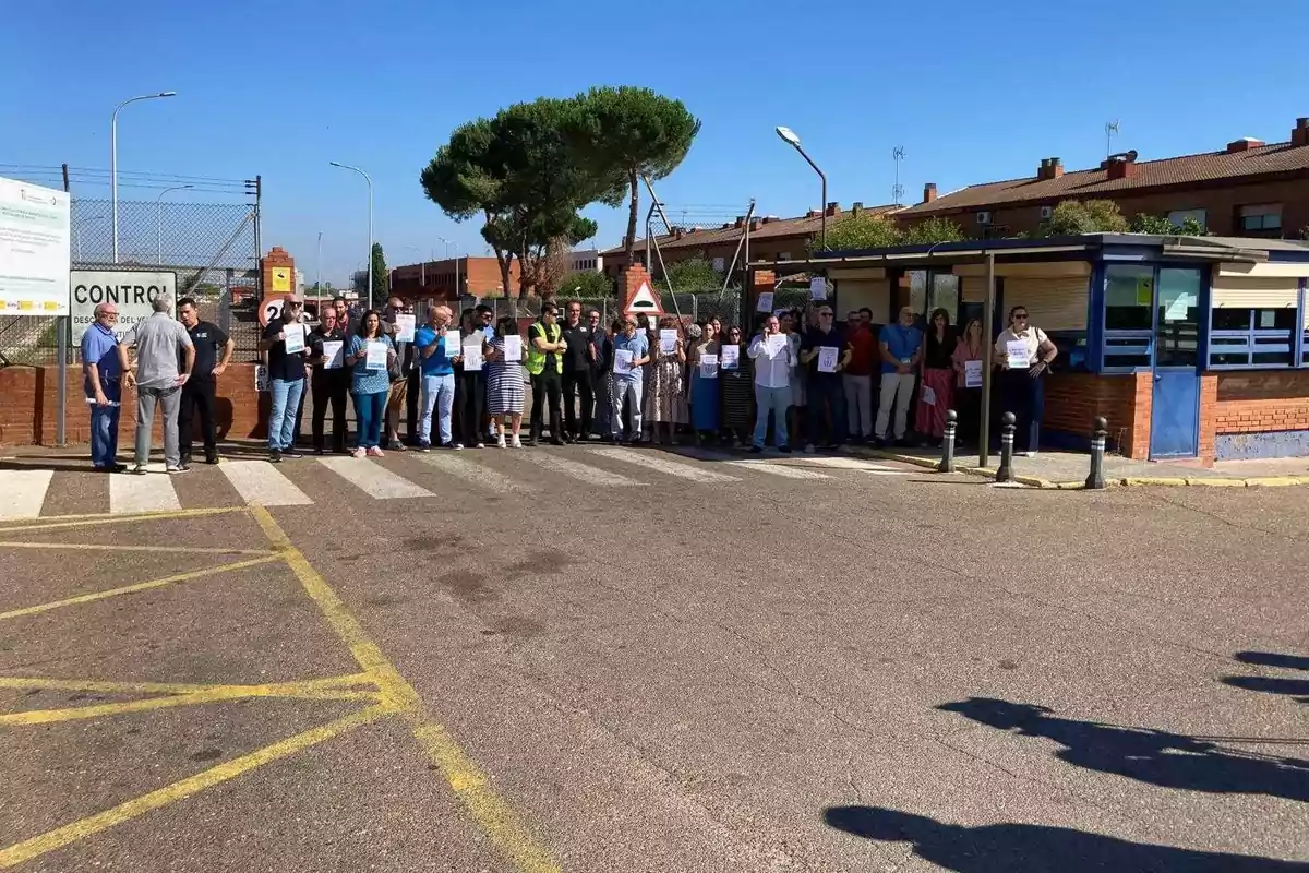 Un grupo de personas está reunido en fila sobre un paso de peatones frente a la entrada de un edificio, muchas de ellas sostienen hojas en las manos y parece un acto de protesta o manifestación bajo un cielo despejado. Un grupo de personas está reunido en fila sobre un paso de peatones frente a la entrada de un edificio, muchas de ellas sostienen hojas en las manos y parece un acto de protesta o manifestación bajo un cielo despejado.