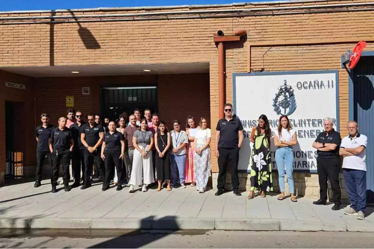 Un grupo de personas posa frente a la entrada de un edificio de ladrillo con un cartel grande que indica Ocaña II y Ministerio del Interior en un día soleado.