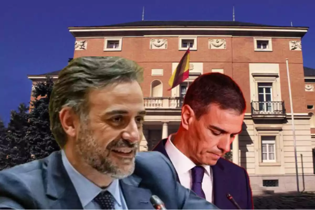 Dos hombres con traje en primer plano frente a un edificio oficial con una bandera de España