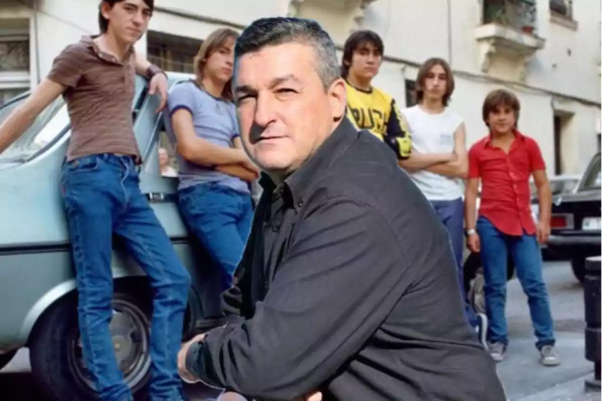 Un hombre de cabello corto y canoso en primer plano con expresión seria, al fondo un grupo de jóvenes de pie junto a un auto en una calle urbana