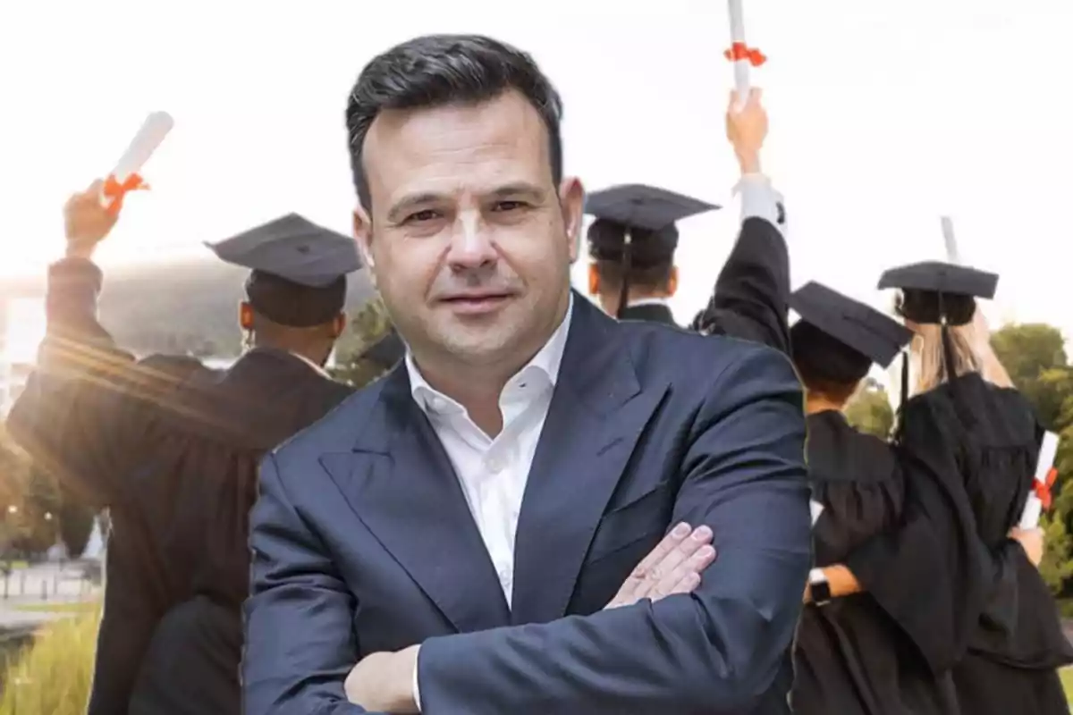 Hombre de traje con los brazos cruzados al frente y grupo de graduados celebrando al fondo