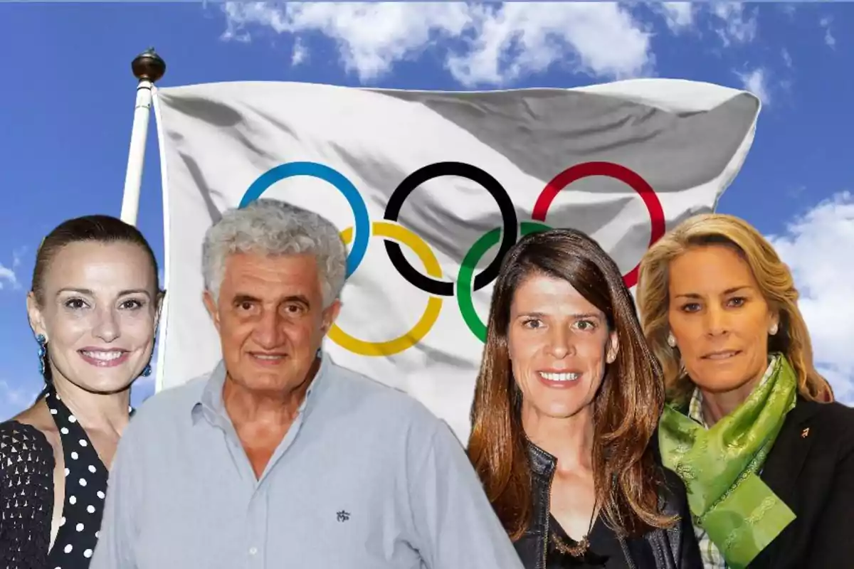 Cuatro personas posan frente a una bandera olímpica ondeando bajo un cielo azul con nubes.