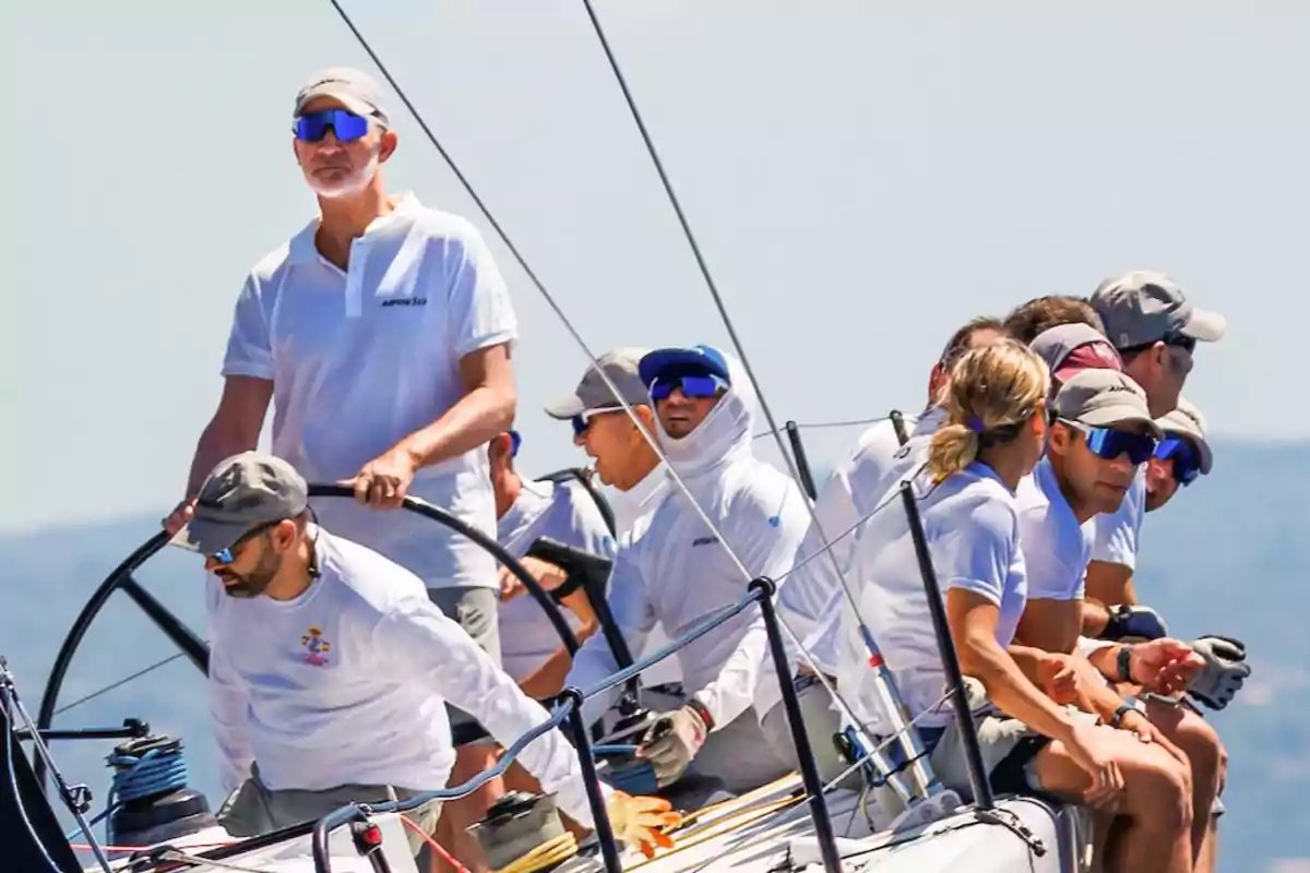 Un grupo de personas con ropa deportiva y gafas de sol navega en un velero durante una competencia en un día soleado