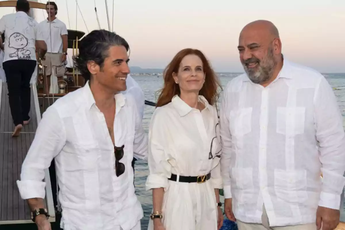 Tres personas sonríen mientras posan juntas en un muelle con el mar de fondo, todas vestidas con ropa blanca y ambiente relajado Tres personas sonríen mientras posan juntas en un muelle con el mar de fondo, todas vestidas con ropa blanca y ambiente relajado