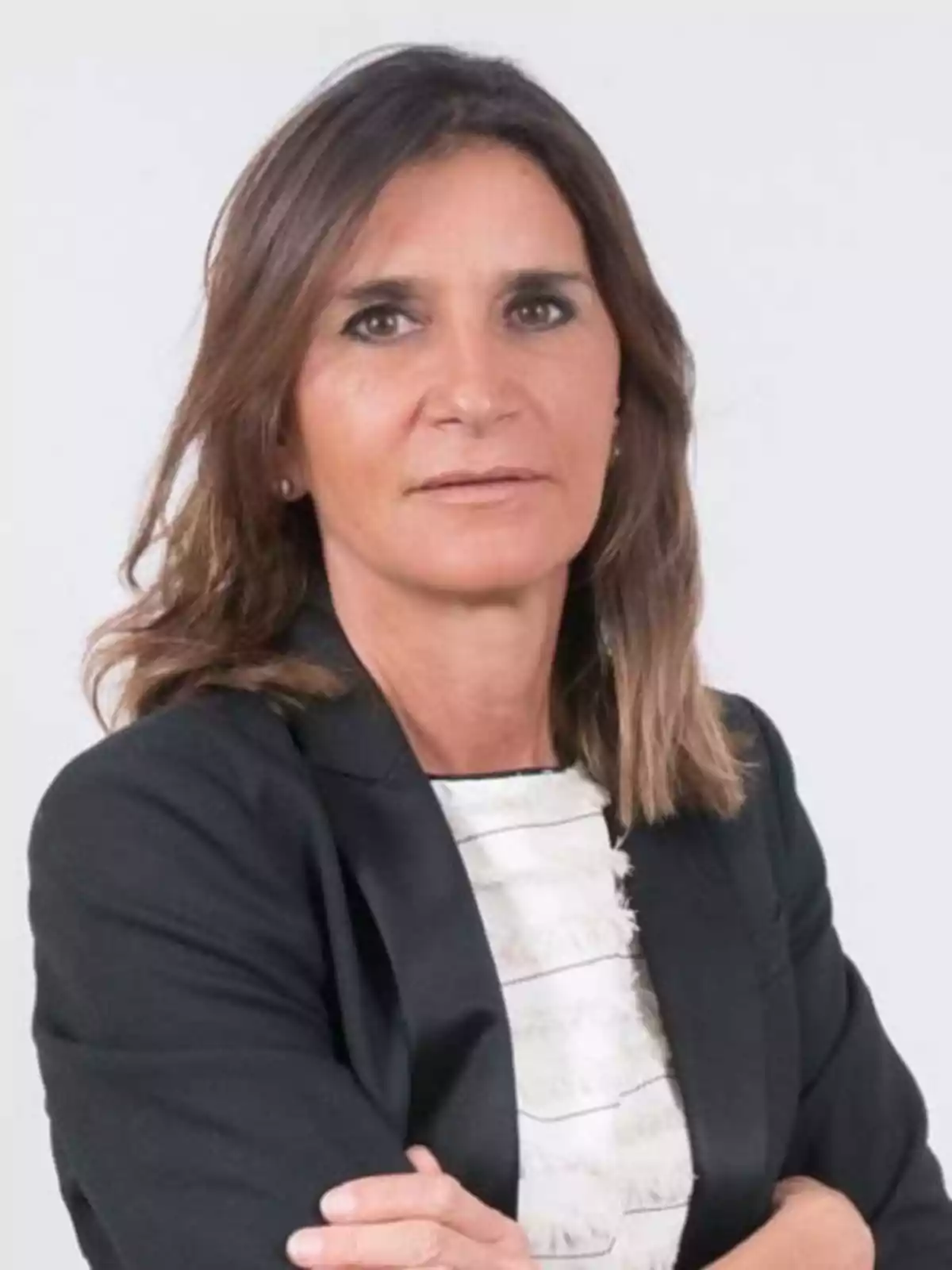 Mujer de cabello castaño y lacio con saco negro y blusa blanca mirando a la cámara con expresión seria Mujer de cabello castaño y lacio con saco negro y blusa blanca mirando a la cámara con expresión seria
