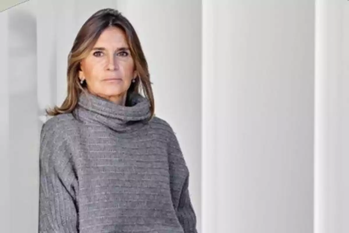 Mujer de cabello castaño y suéter gris posando frente a un fondo blanco Mujer de cabello castaño y suéter gris posando frente a un fondo blanco