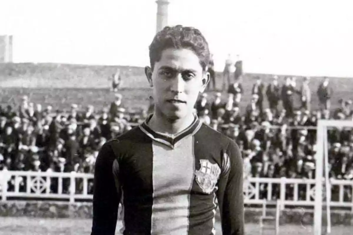 Joven futbolista con uniforme antiguo de rayas verticales posando en un campo de fútbol con público en las gradas al fondo Joven futbolista con uniforme antiguo de rayas verticales posando en un campo de fútbol con público en las gradas al fondo