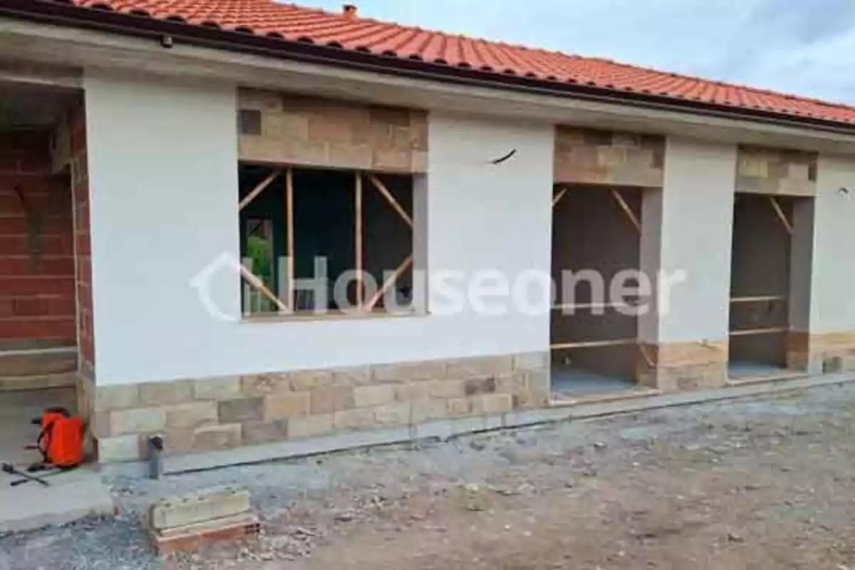 Fachada de una casa en construcción con paredes blancas, detalles de piedra en la parte inferior y techo de tejas rojas Fachada de una casa en construcción con paredes blancas, detalles de piedra en la parte inferior y techo de tejas rojas